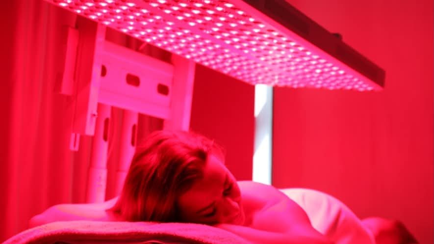 A client lying face down on the treatment table with the red and near-infrared panel positioned above the back and shoulders