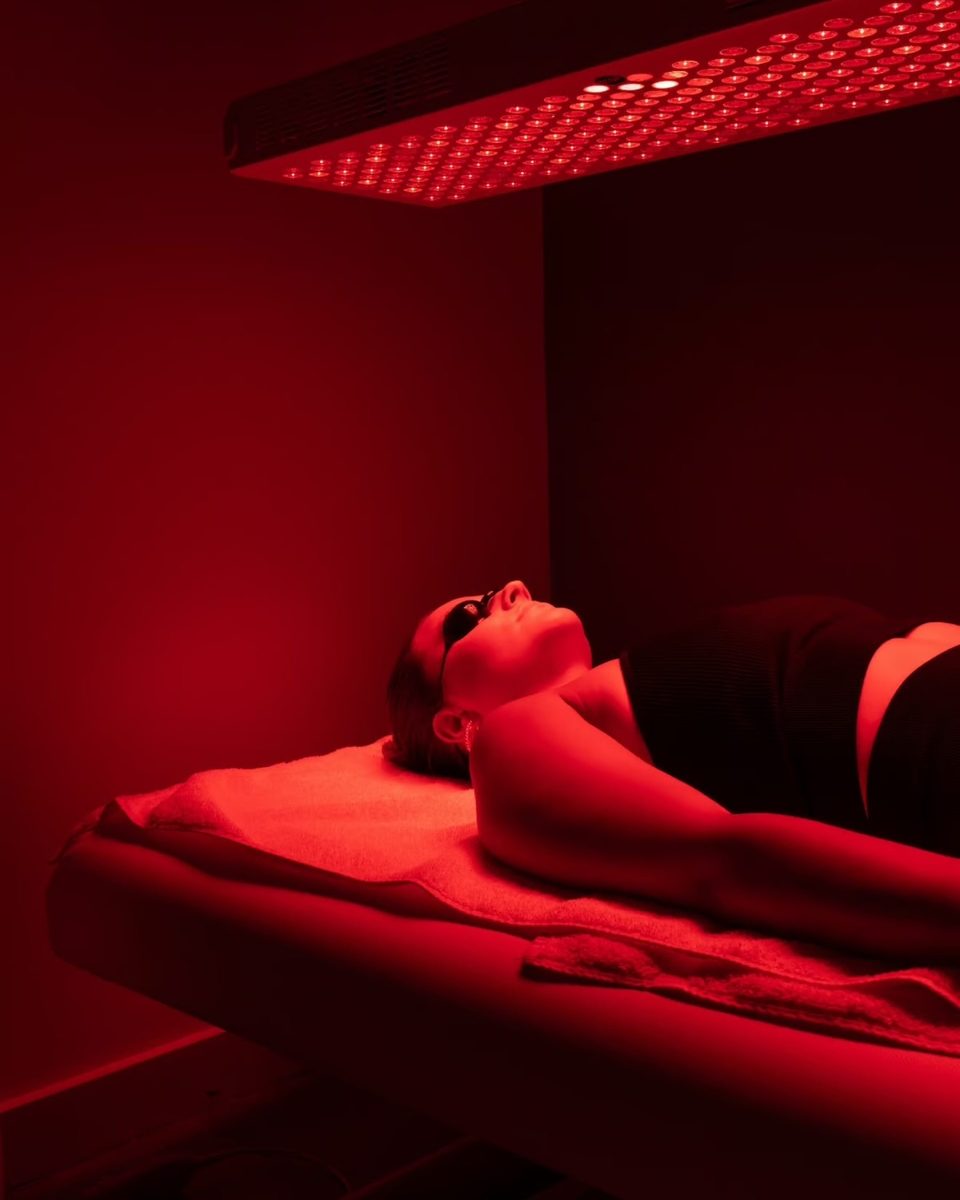 A client lying on the treatment table at ReVibe Centre with the red and near-infrared panel angled above them, the room lit deep red