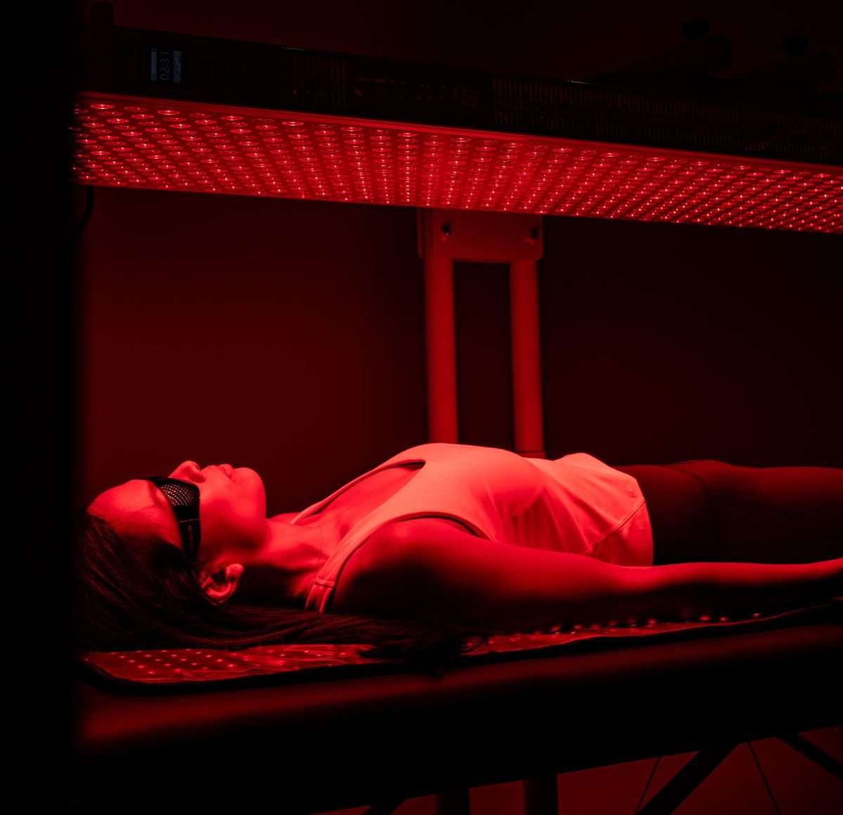 A client lying on the treatment table at ReVibe Centre under the full-body red and near-infrared panel, wearing protective goggles